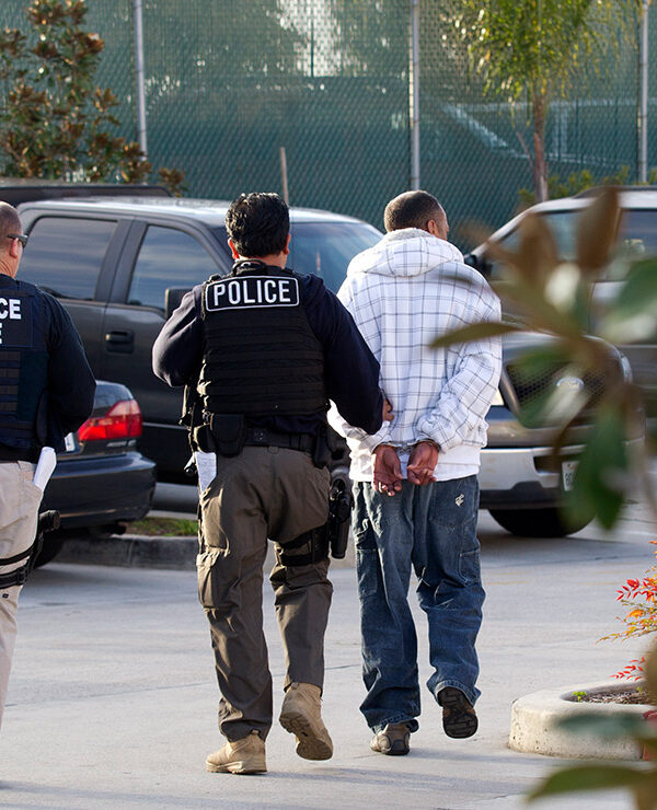 Two Immigration and Customs Enforcement (ICE) agents take a person into custody