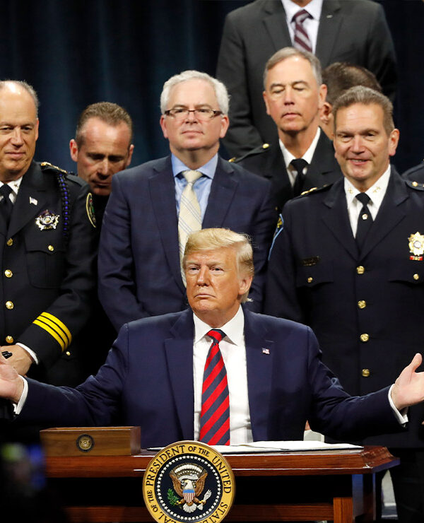 President Trump sits at podium ready to sign executive order creating a commission to study law enforcement and justice, surrounded by officers beside him in support.