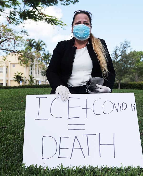 A woman wears a protective face mask and gloves as she protests outside of a U.S. Immigration and Customs Enforcement field office Friday, May 29, 2020, in Plantation, Fla.