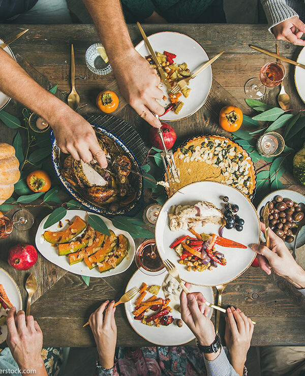 Flat-lay of friends feasting at Thanksgiving Day table with turkey, pumpkin pie, roasted seasonal vegetables and fruit, top view