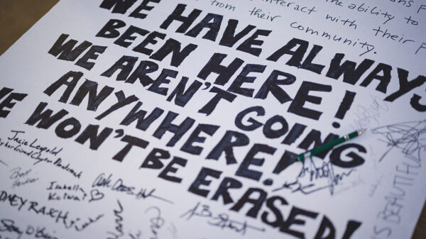 A demonstration poster that reads “We Have Always Been Here! We Aren’t Going Anywhere! We Won’t Be Erased.”