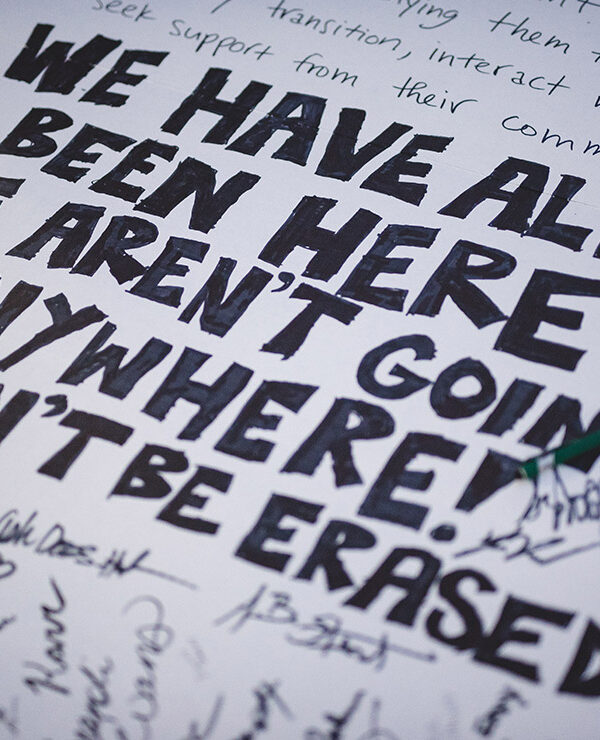 A demonstration poster that reads “We Have Always Been Here! We Aren’t Going Anywhere! We Won’t Be Erased.”