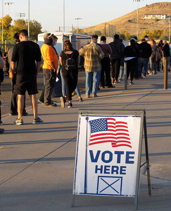 A sign that says "vote here" among a line of voters.
