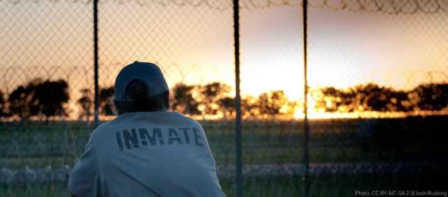 Inmate staring off into a field behind a fence