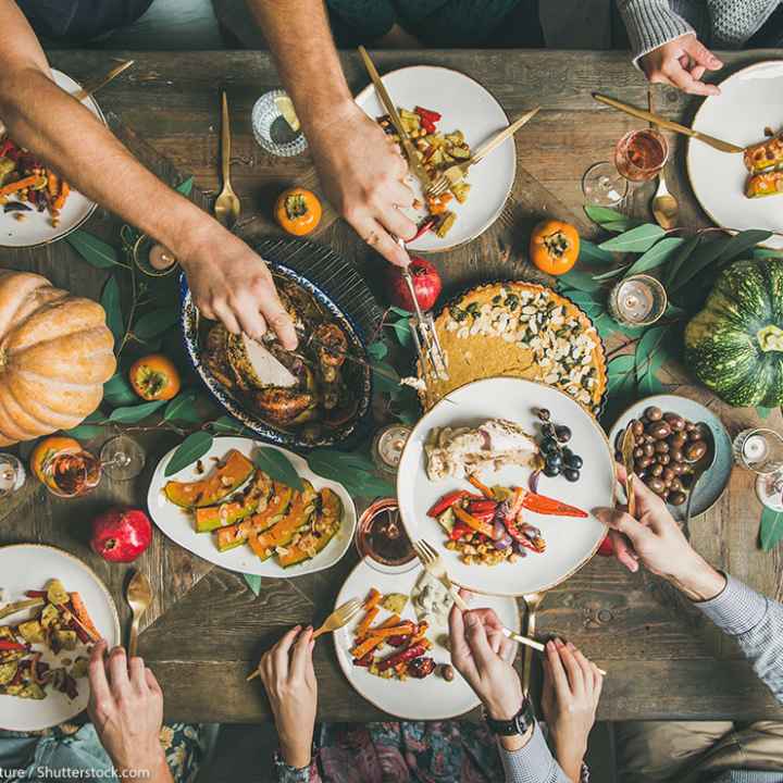 Flat-lay of friends feasting at Thanksgiving Day table with turkey, pumpkin pie, roasted seasonal vegetables and fruit, top view
