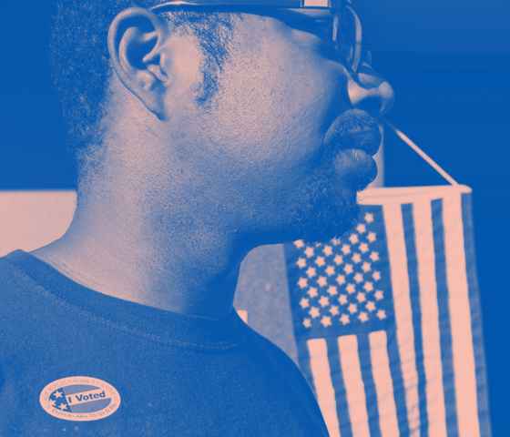 A man wears an "I Voted" stick with the American flag hanging in the background. Image tinted blue and pink.